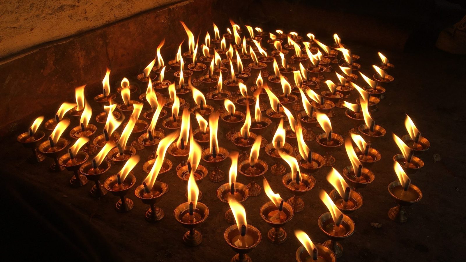 Rows of lit oil lamps in warm amber darkness