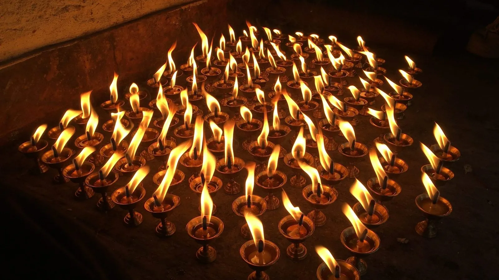 Rows of lit oil lamps in warm amber darkness