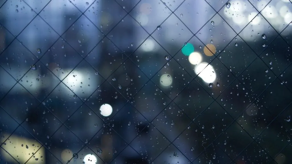 Raindrops on a night window with cold blue city lights